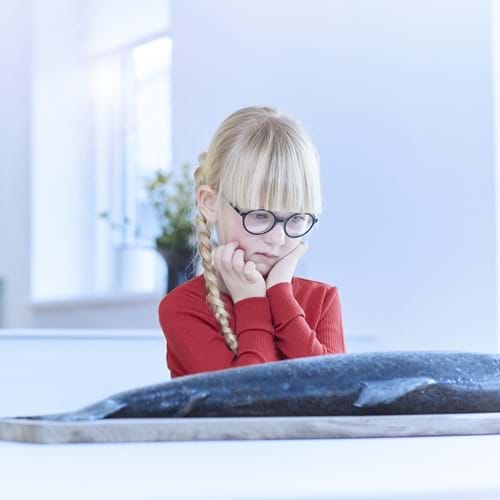 Pige med cerebral parese kigger undrende på laks, der ligger på bordet